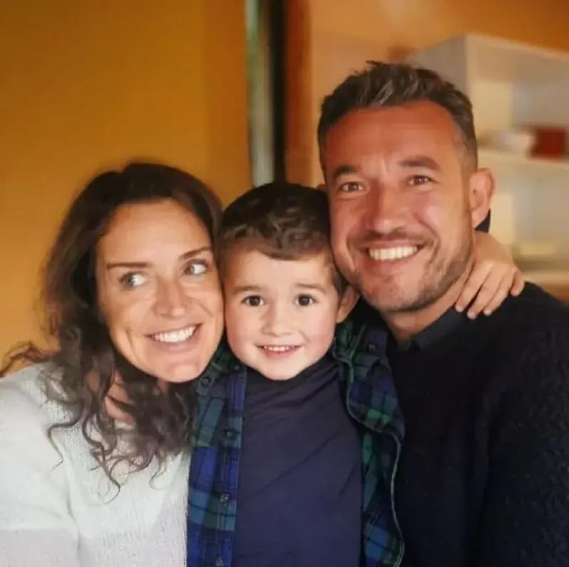 Tom Williams smiling cheek to cheek with his wife and their young son.